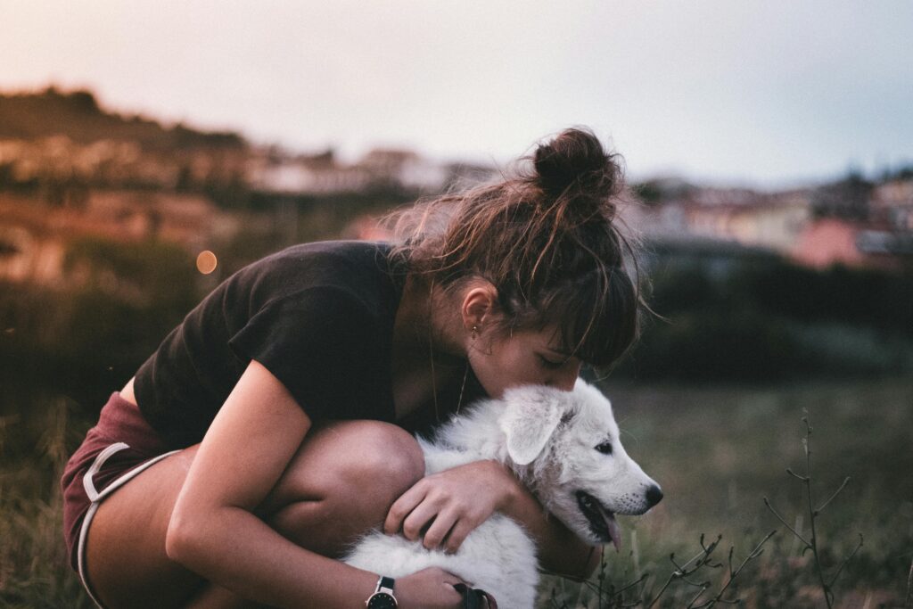 A young woman lovingly embraces her white dog in Tuscany's scenic landscape.